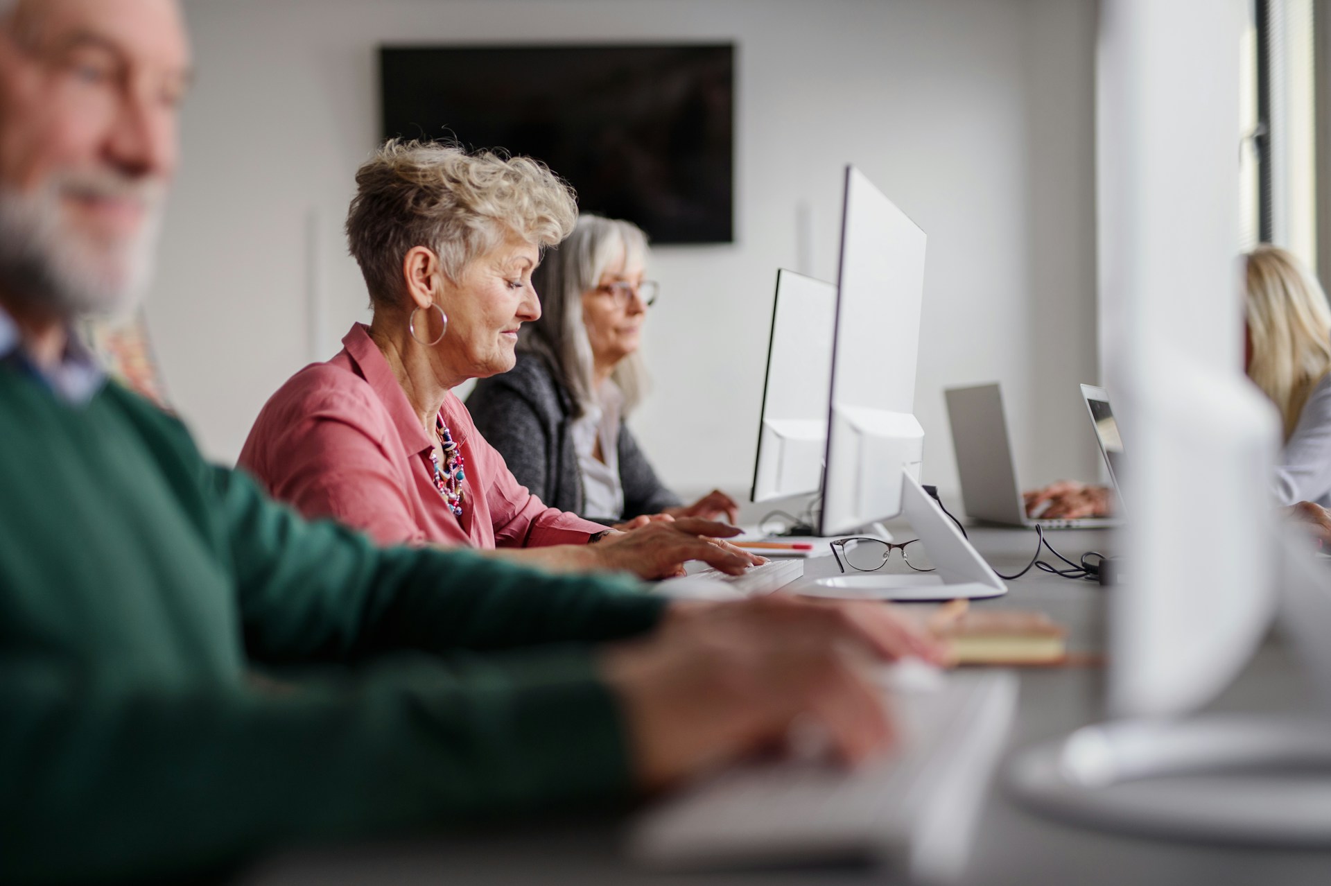 A row of older adults at desktop computers in a bright office, working through numbers on screen